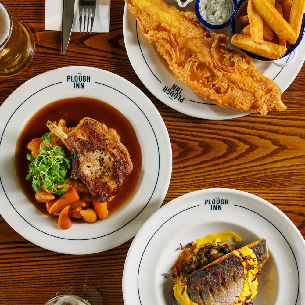 Three dishes including fish and chips, pork chop and seabass from The Plough's food and drink menu.